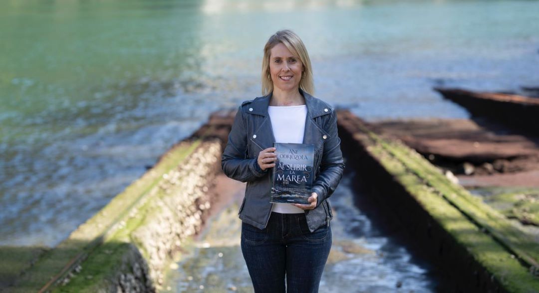 Imagen de Ane odriozola, con un fondo fluvial, y su libro en la mano.