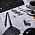 En una mesa boligrafos, pendrive, cafe, calculadora, ratón, ordenador y clips