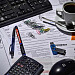 En una mesa boligrafos, pendrive, cafe, calculadora, ratón, ordenador y clips